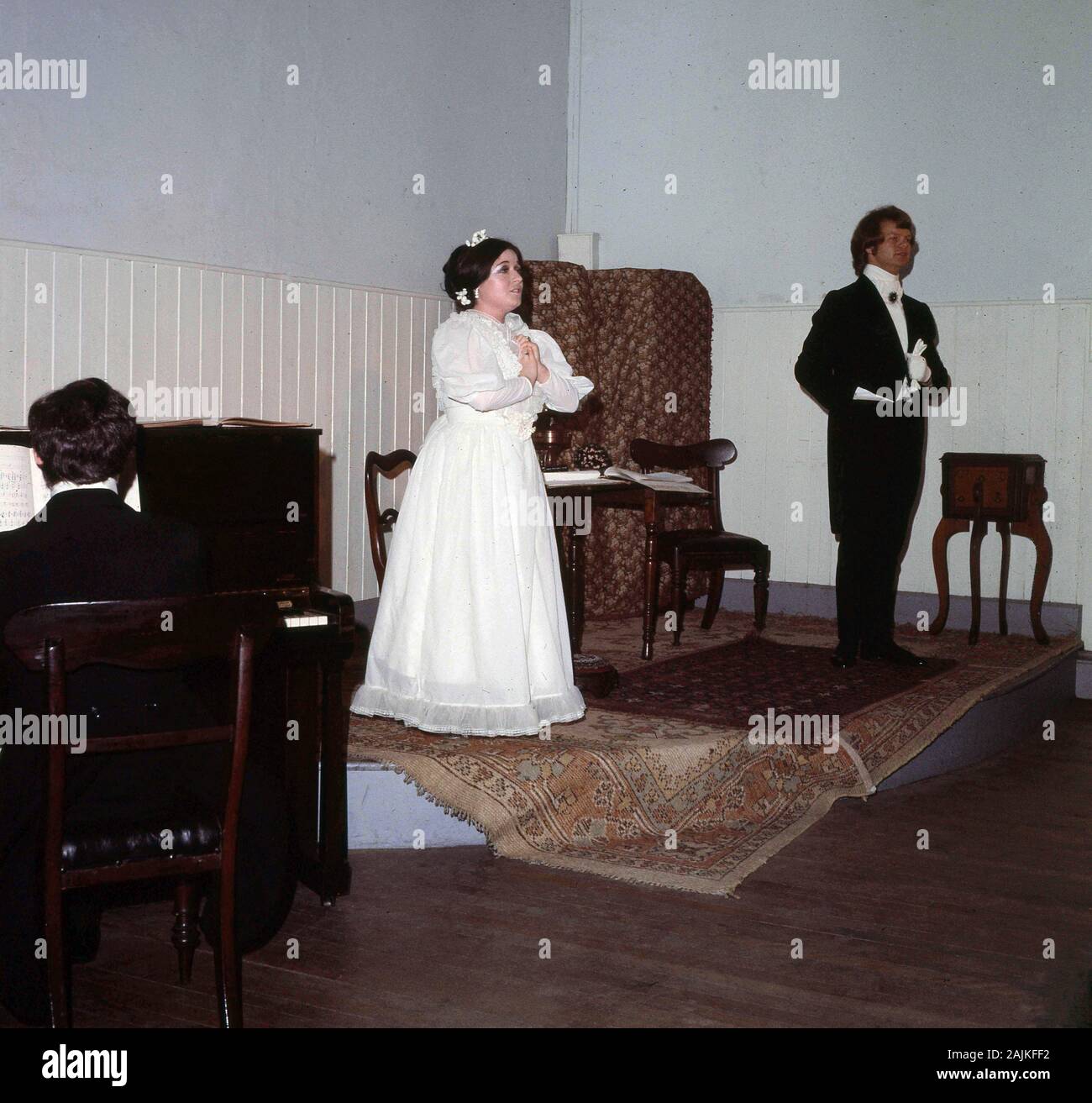 1960er Jahre, historisch, ein Trio, das in Wexford, Irland, auftrat, mit einem Mann und einer Frau in schwarzem Krawattenkostüm auf einer kleinen Bühne, die einem viktorianischen Vorraum ähnelte und zusammen sang, begleitet von einem Mann, der ein Klavier spielte. Stockfoto