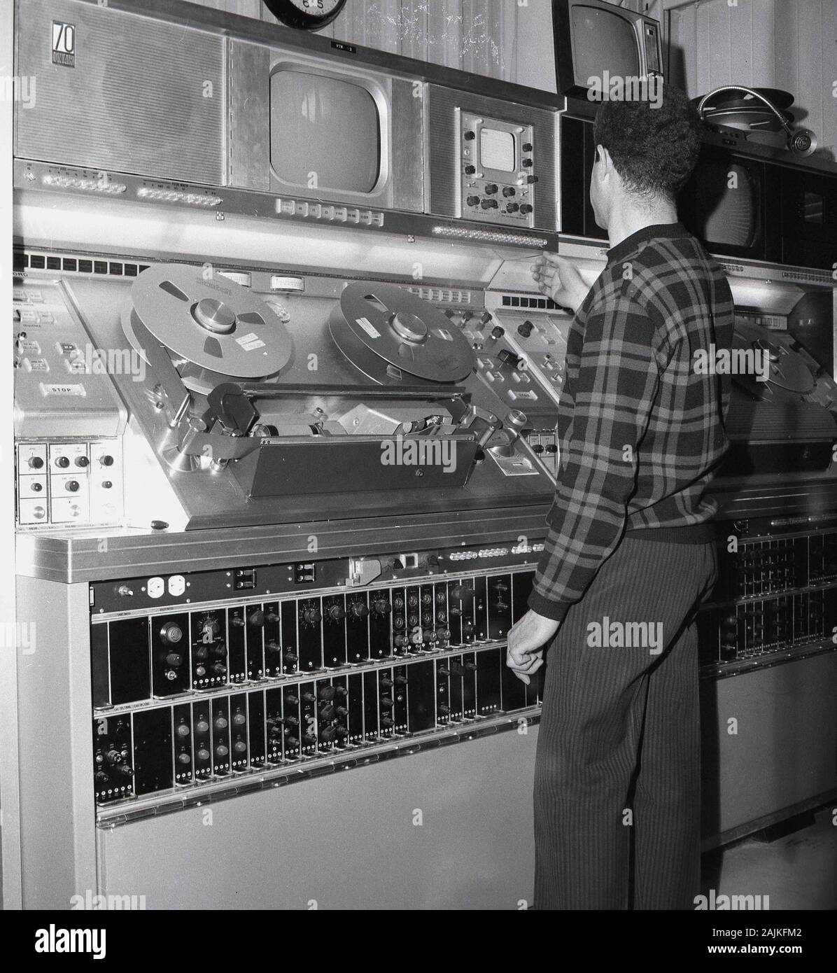 1960er Jahre, historisch, ein männlicher Techniker, der an der Sendeanlage in einer Fernsehraum in Saudi-Arabien arbeitet. In dieser Ära wurden analoge Geräte verwendet, die auf Band mit 2-Zoll-Videorekordern und Playern für die Übertragung und Aufzeichnung basieren. Das 2-Zoll-Videoband wurde Mitte der 50-er Jahre entwickelt und war das erste praktische und kommerziell erfolgreiche Videoformat für analoge Aufnahmen. Stockfoto