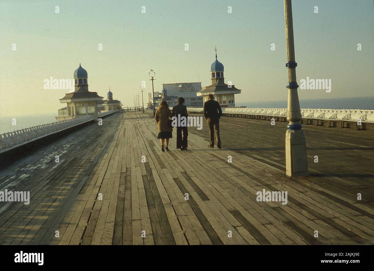 1960er Jahre, historisch, zwei Männer und eine Frau auf der Holzdecke am North Pier, Blackpool, Lancashire, England. In der Ferne, der Pavillon des Piers, in dem Bernard Delfonts 'Showtime', ein Unterhaltungsspektakel, aufgeführt ist, das von den späten 1950er bis zu den frühen 1980er Jahren lief und viele der größten Namen im Showbusiness aufwies. Stockfoto