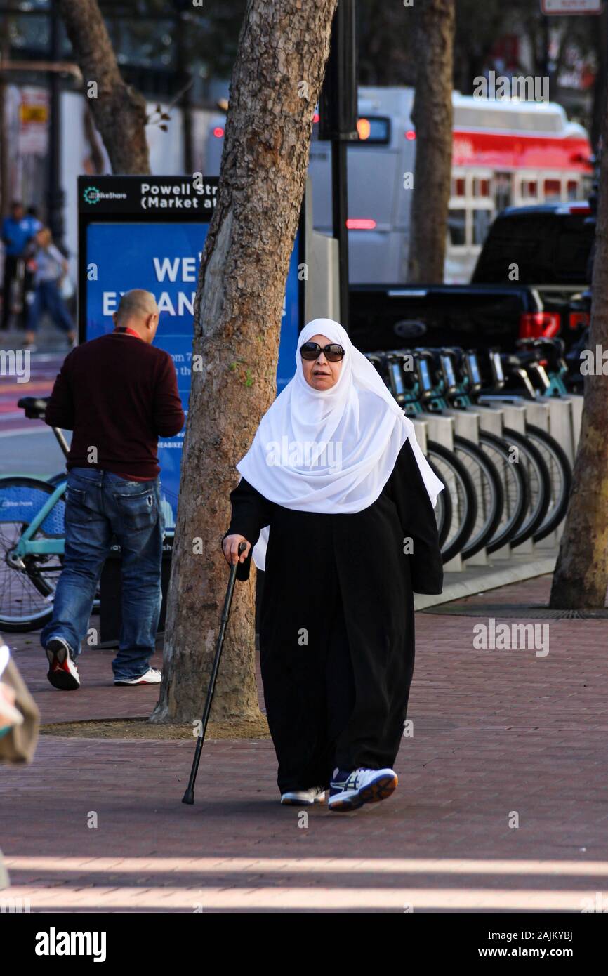 Ältere Frau mit Sonnenbrille, weißen Schal und Spazierstock auf Bürgersteig Stockfoto