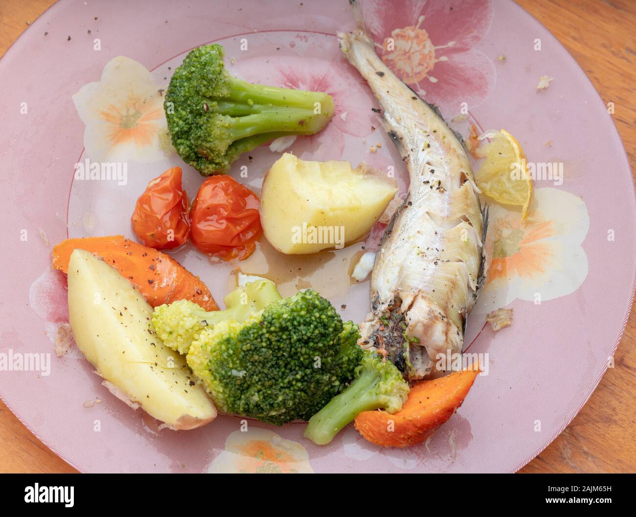 Geschmorte Pollock mit Kartoffeln, Kohl, Brokkoli und Tomaten auf rose Platte mit Stück Zitrone Stockfoto