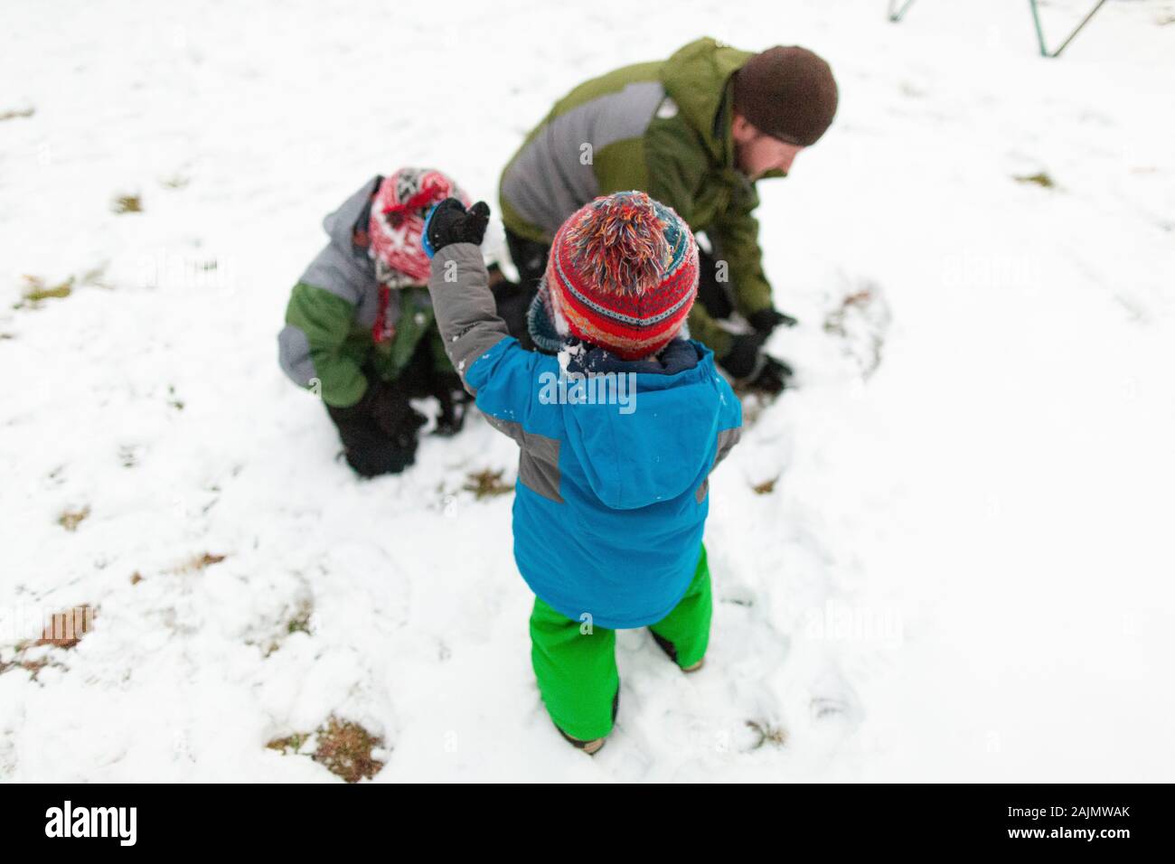 Vater macht einen Schneeball draußen mit zwei Kindern im Winter Stockfoto