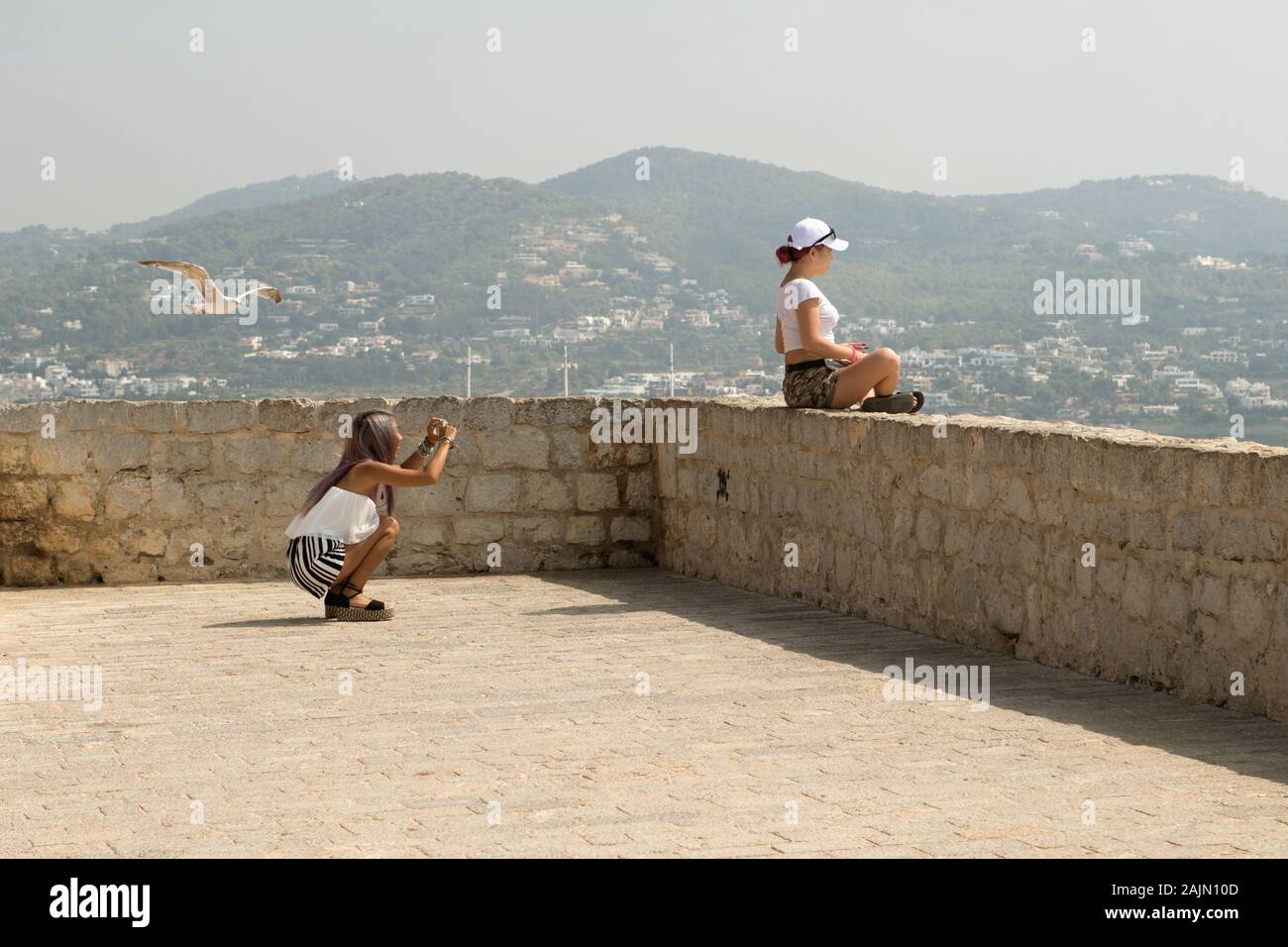 Eine touristische kauert, ein Foto von ihrem Freund an der Spitze von Eivissa (Ibiza) als eine Möwe swoops Vergangenheit über den Schuß zu ruinieren, Stockfoto