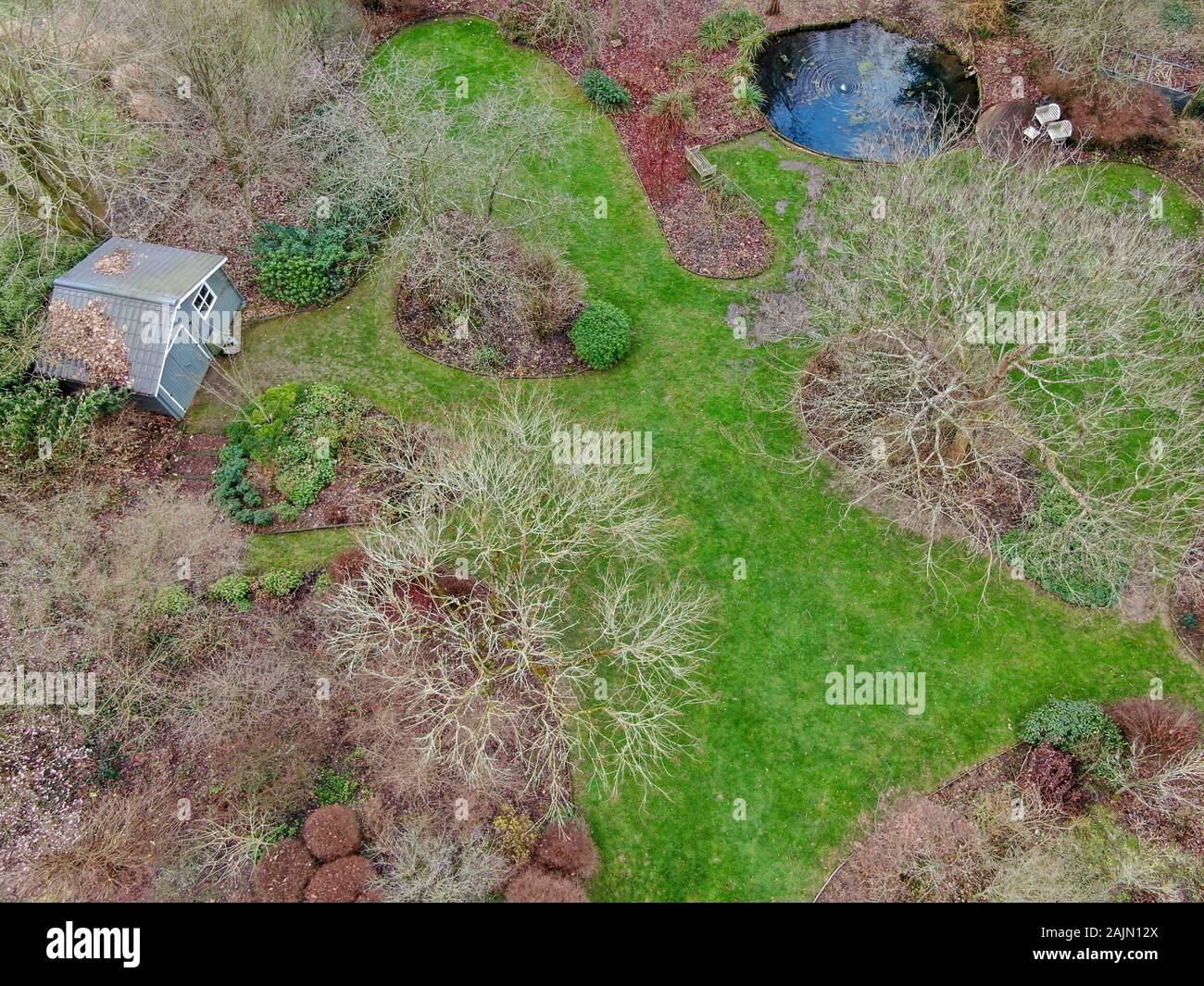 Luftbild des Englischen Garten Typ während der Wintersaison. Garten mit einem großen grünen Gras, wenig Pfund Wasser und verschiedene Pflanzen, Bäumen und kleinen Garten Haus aus Holz. Stockfoto