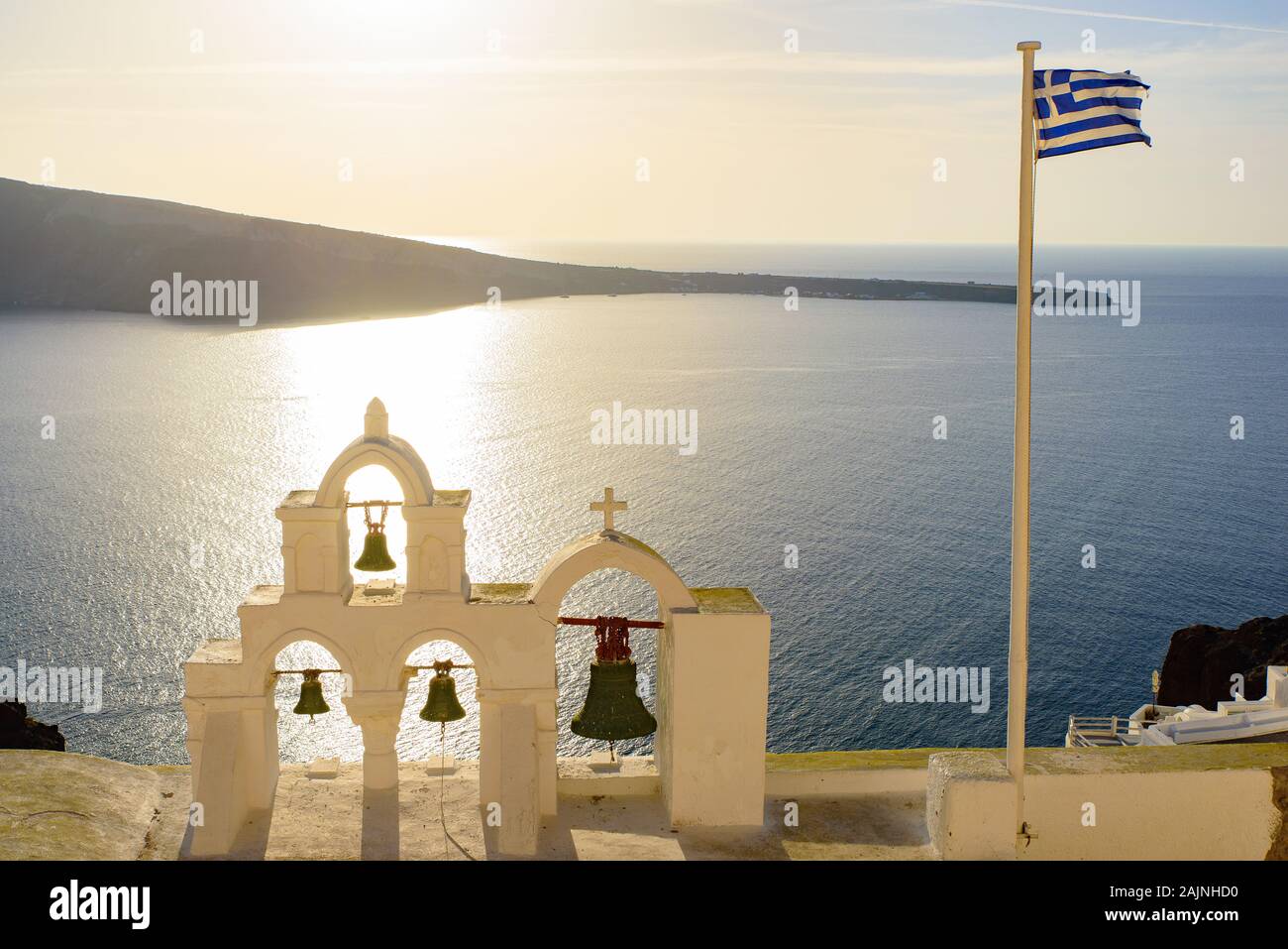 Glockenturm und Nationalflagge von Griechenland im Sonnenuntergang in Oia, Santorini, Griechenland Stockfoto