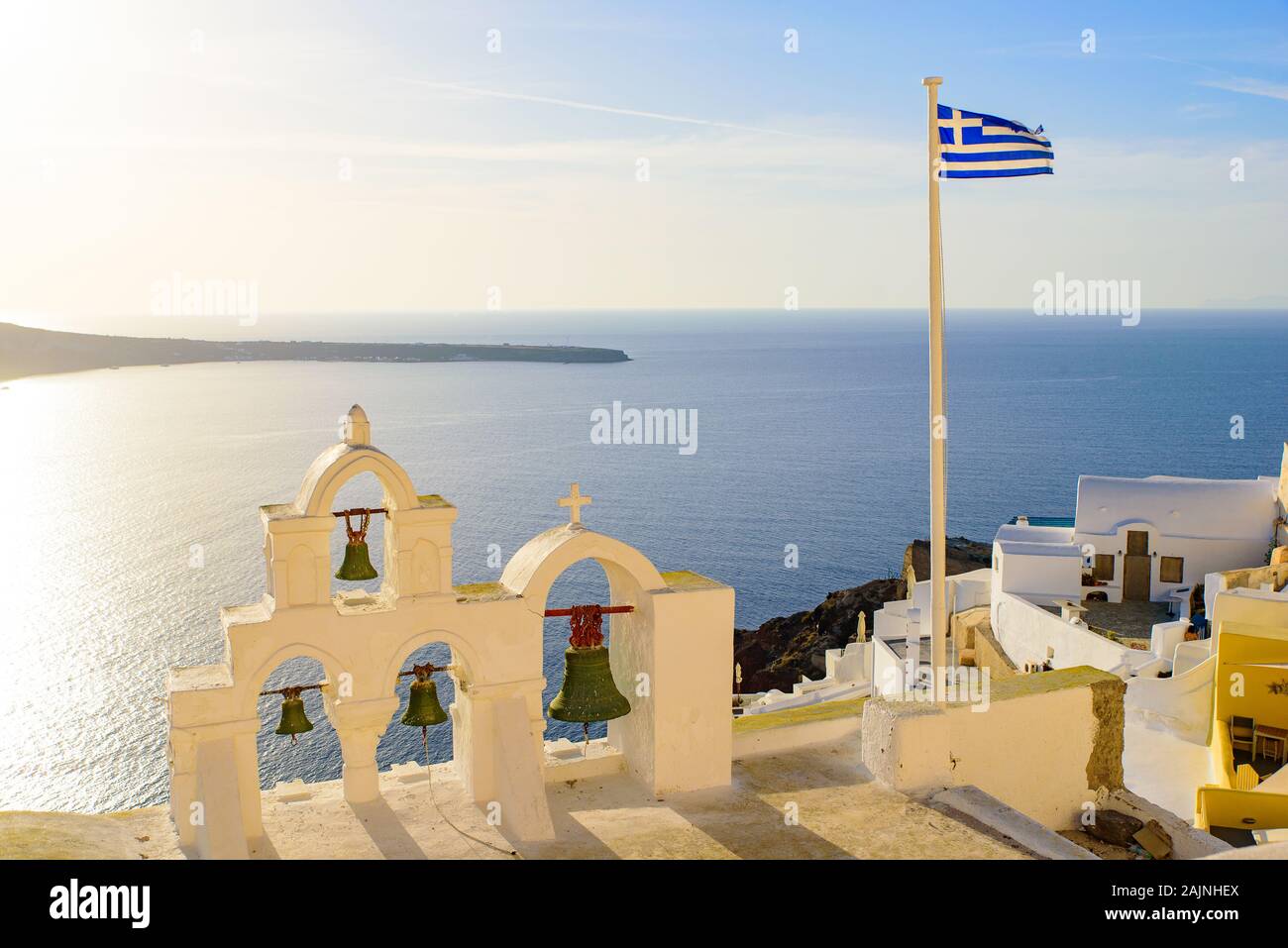 Glockenturm und Nationalflagge von Griechenland im Sonnenuntergang in Oia, Santorini, Griechenland Stockfoto