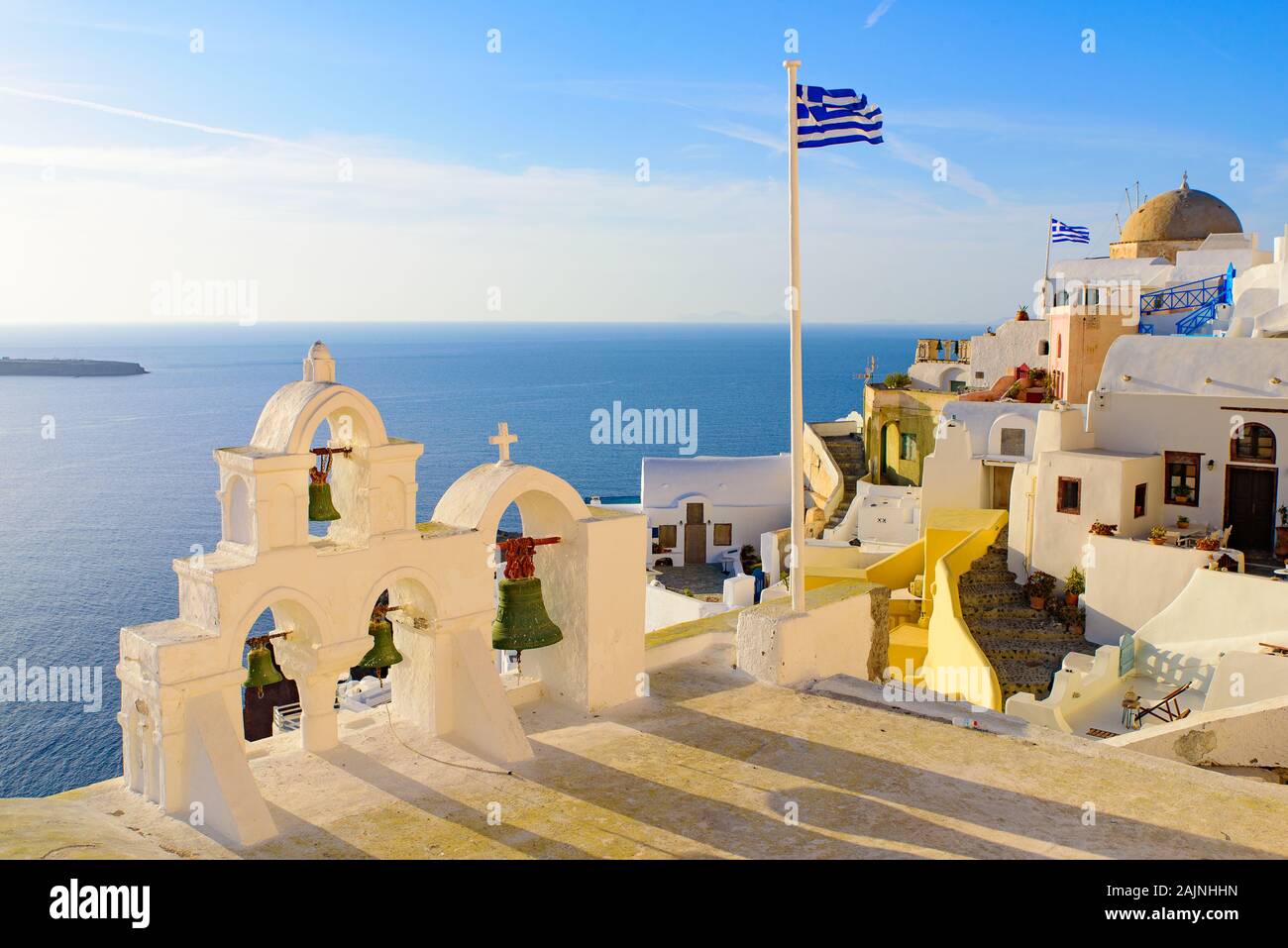 Glockenturm und Nationalflagge von Griechenland im Sonnenuntergang in Oia, Santorini, Griechenland Stockfoto