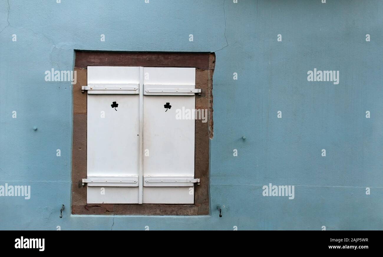 Vintage geschlossenes Fenster mit weißen Fensterläden aus Holz auf einem hellblauen Wand Stockfoto
