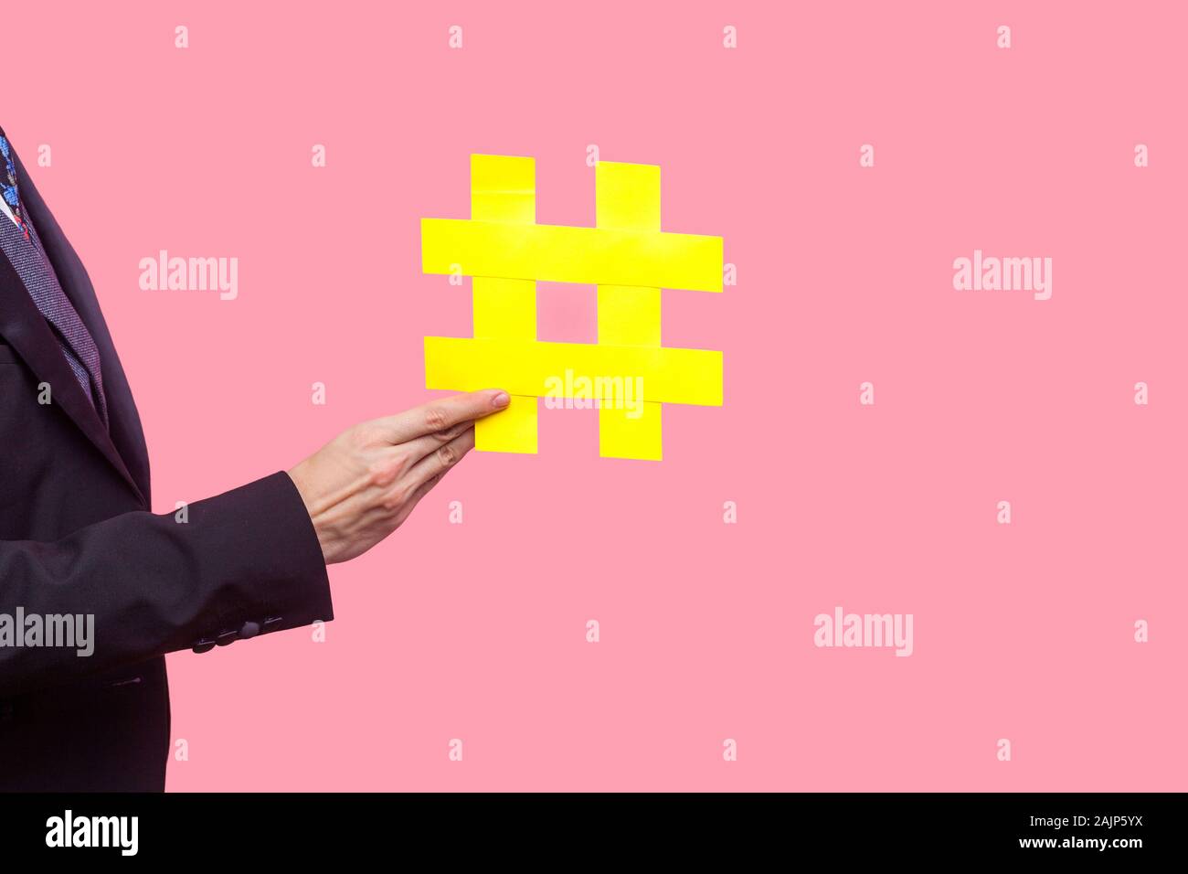 Nahaufnahme der männlichen Hand in eleganten schwarzen Tuxedo mit großen gelben hashtag Symbol, Popularität und Förderung in Social Media, viral Content, Trending. Ich Stockfoto