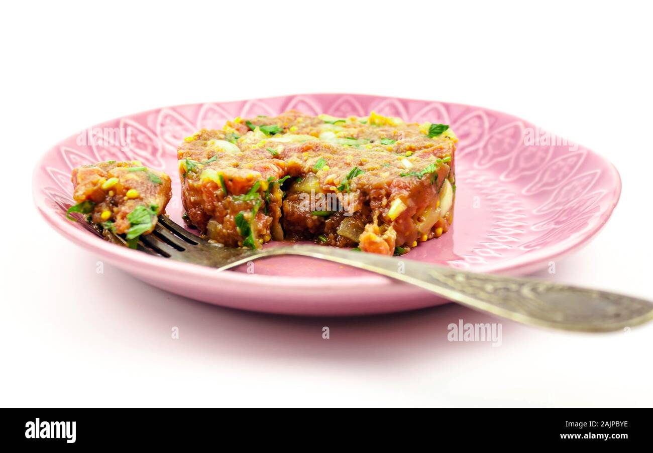 Beef Tartare kalte Vorspeise rosa Teller rohes Hackfleisch mit Eigelb, Zwiebeln, Kräuter, Olivenöl, Zitronensaft, Gewürze auf weißem Hintergrund Nahaufnahme. Sel Stockfoto