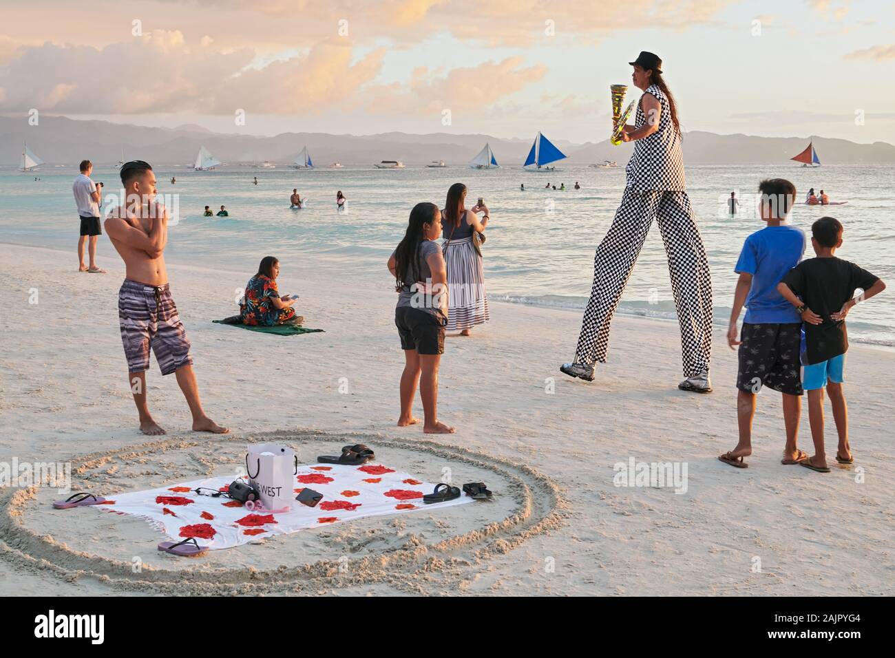 , Aklan Boracay, Philippinen: Mann auf Stelzen, Jonglieren entlang der weißen Strand bei Sonnenuntergang, mit lokalen Touristen als Zuschauer. Stockfoto