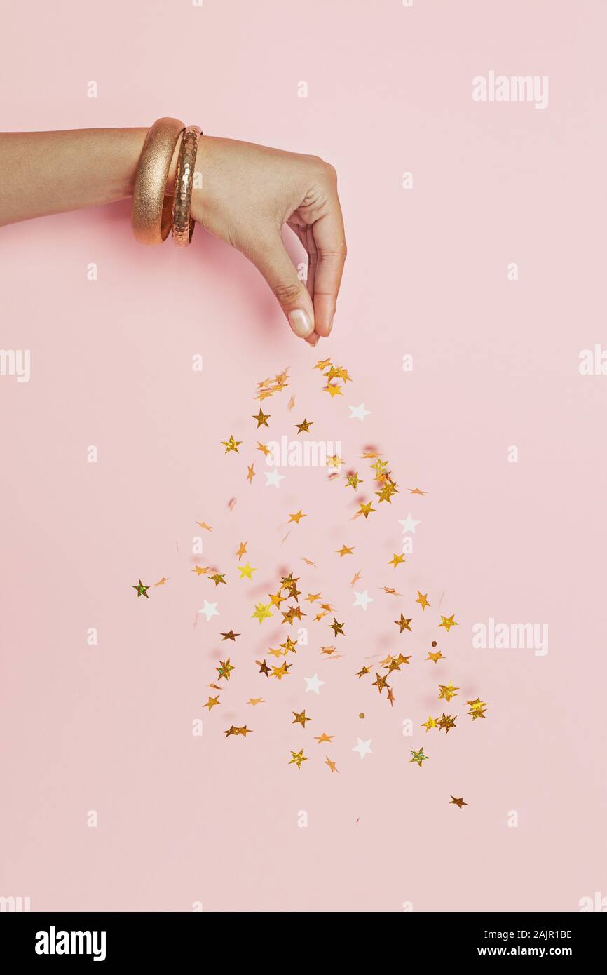 Schöne weibliche Hand streams funkelnden Gold Sterne Konfetti auf rosa Hintergrund Stockfoto