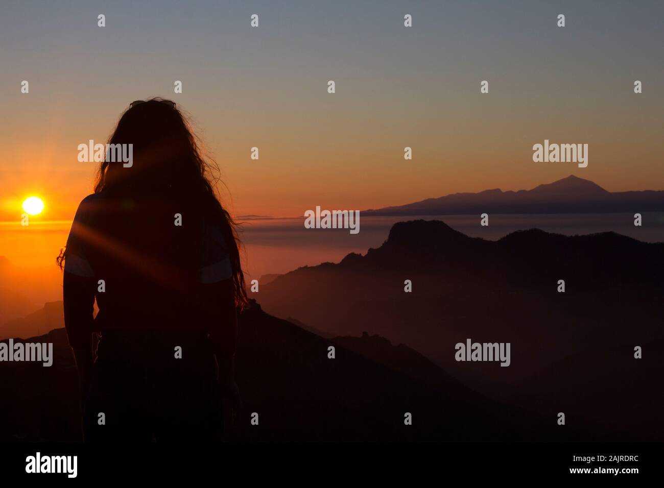 Weibchen mit langem Hören, während sie auf dem Berg steht, den Sonnenuntergang betrachten Stockfoto