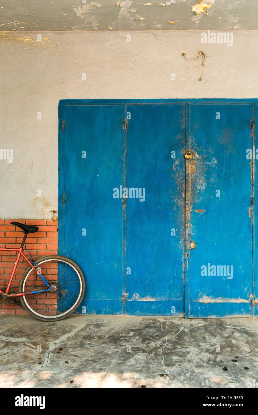 Rotes Fahrrad, das an der Wand in der Nähe der alten rostigen blauen Tür in Morondava, Madagaskar, gelehnt ist Stockfoto