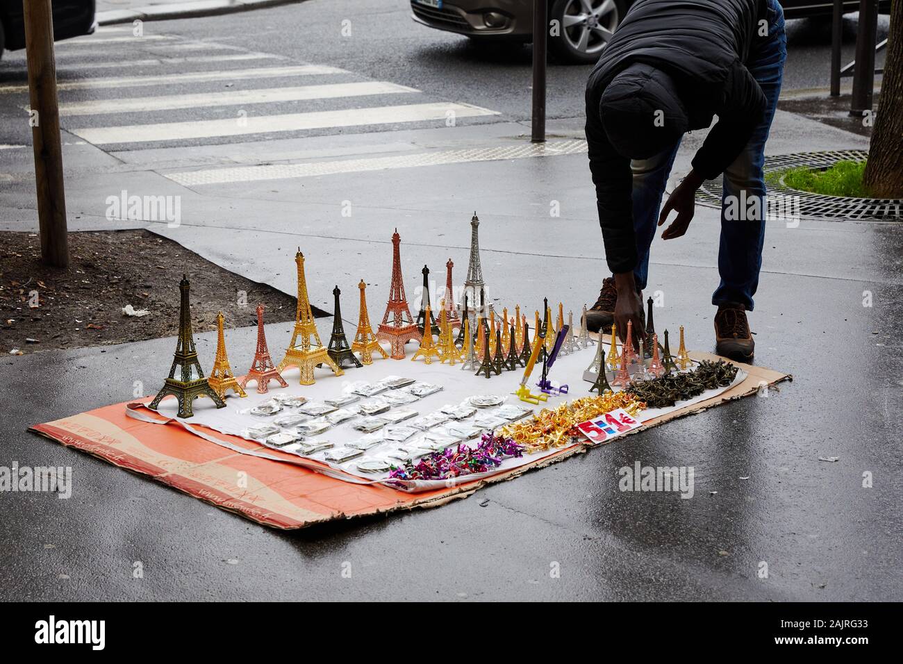 Mann verkauf Miniatur Eiffel Towers, ausgebreitet auf einem Stück Karton auf einer nassen Straße; Paris, Frankreich Stockfoto