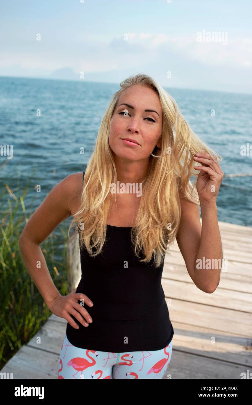Porträt der blonden Frau, die schwarze Oberseite an einem See trägt, mit Blick auf die Kamera. RF Outdoor-Lifestyle-, Freizeit-/Urlaubskonzept, mit Modellfreigabe (MR) Stockfoto