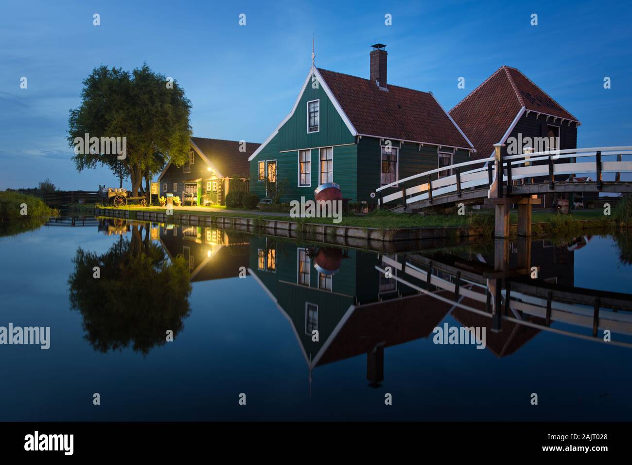 Traditionelle Käserei im Grün mit einer Brücke mit dem Spiegelbild im Wasser in Zaanse Schans, die Niederlande in der blauen Stunde in der Dämmerung. Stockfoto