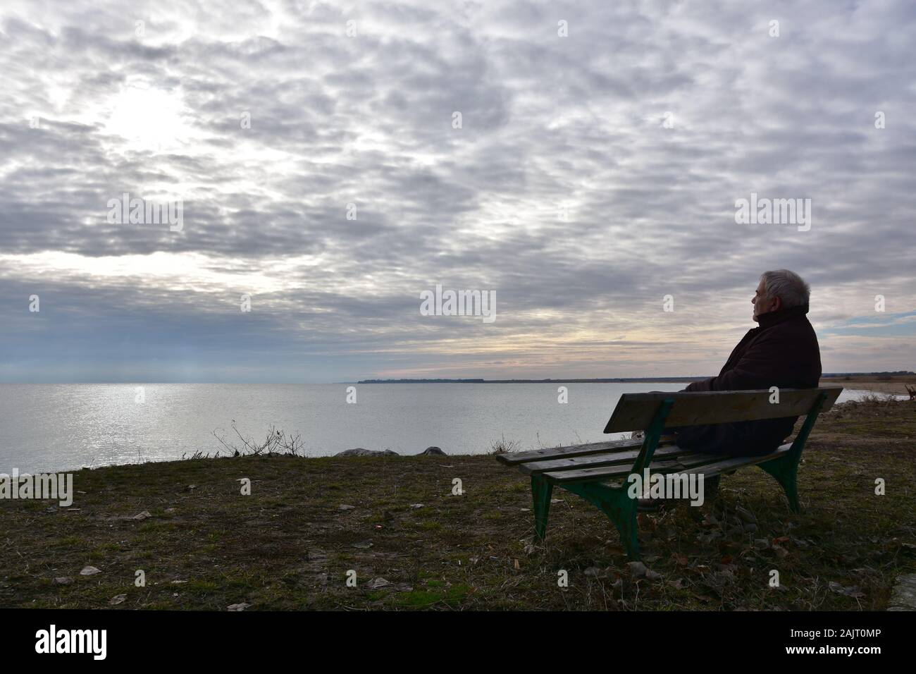 Silhouette der Mann über 50 Jahre sitzen auf einem alten Holzbank, über die in einem trüben Wintertag. Ältere Menschen beobachten die in nostalgische Stimmung siehe Stockfoto