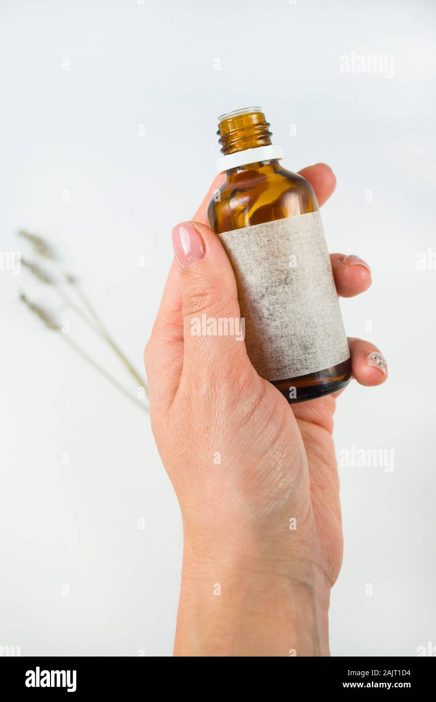 Hausgemachte Hautpflege Kosmetik. Ätherisches Öl in Lady's Hand n weißen Hintergrund mit Kräutern. Organische selfcare Konzept. Stockfoto