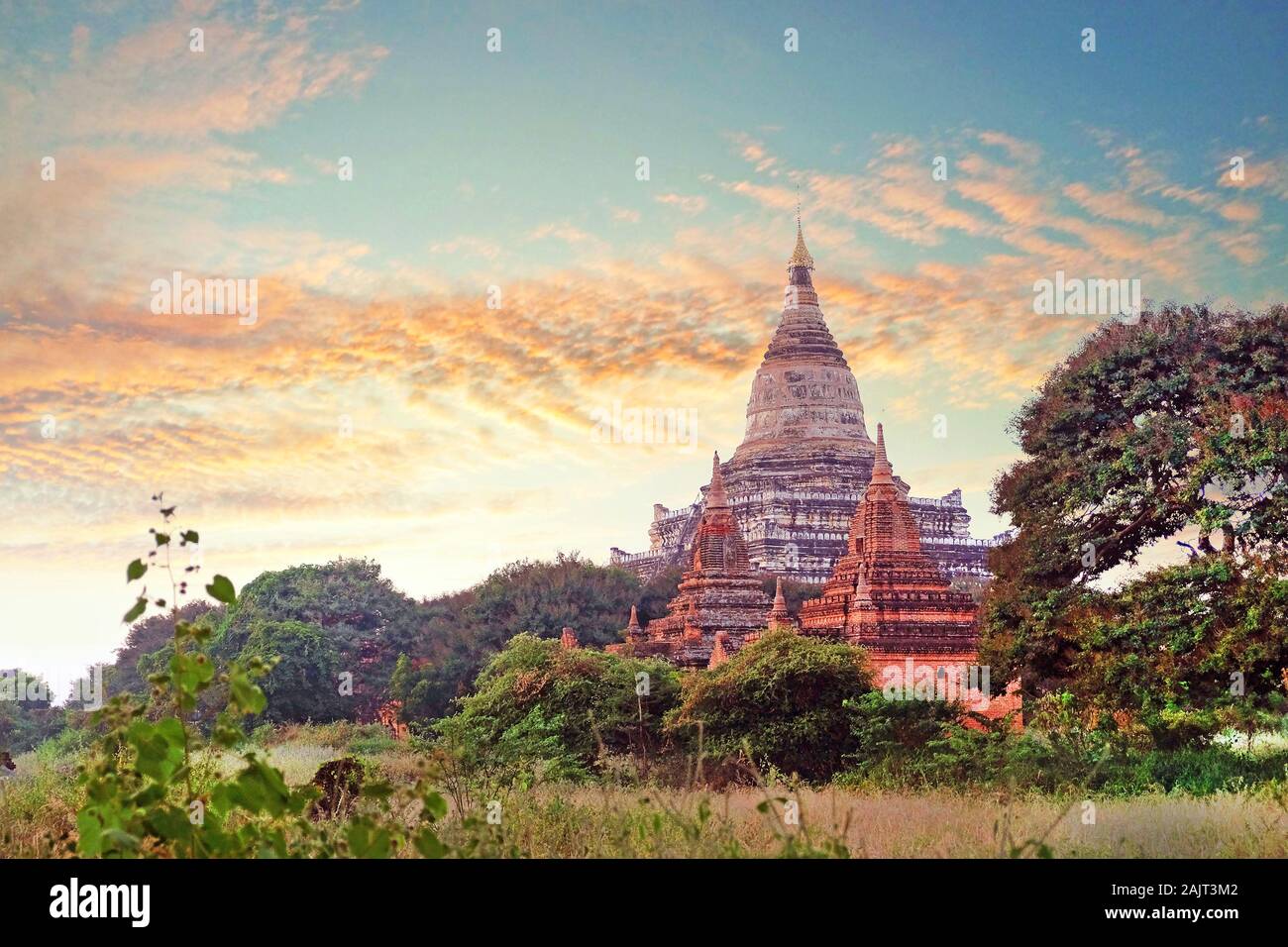 Bunte warmen Sonnenuntergang Himmel über alte buddhistische Tempel von grüner Vegetation im Old Bagan, Myanmar umgeben. Stockfoto