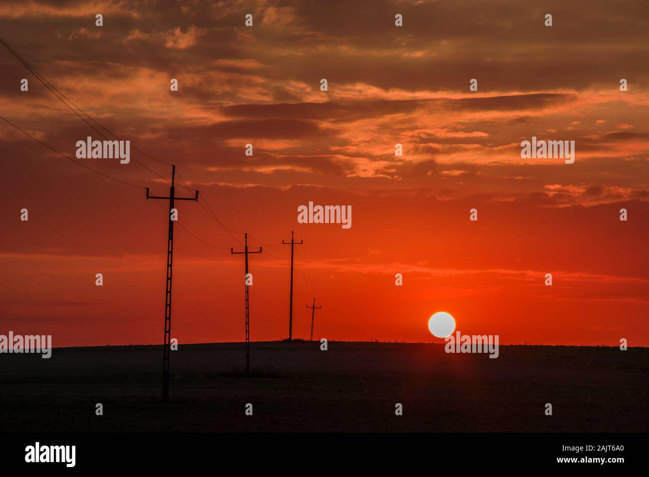 Roter Sonnenuntergang mit Wolken und elektrischen Polen im Feld. Staw, Polen Stockfoto