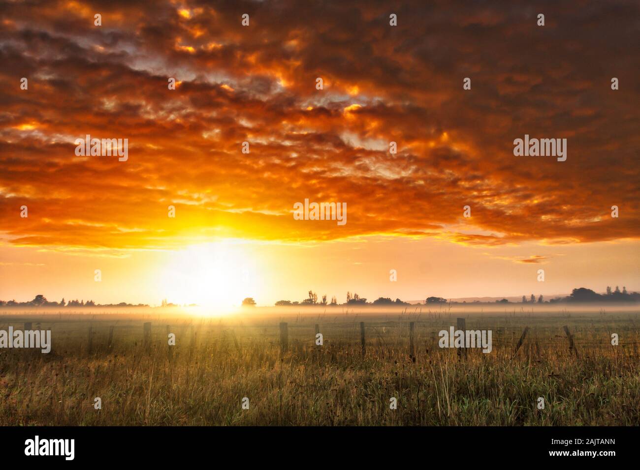 Dramatische lebendige cloudscape bei Dämmerung über Dunst und Nebel mit einer Sonne flare am Horizont auf der Farm Stockfoto