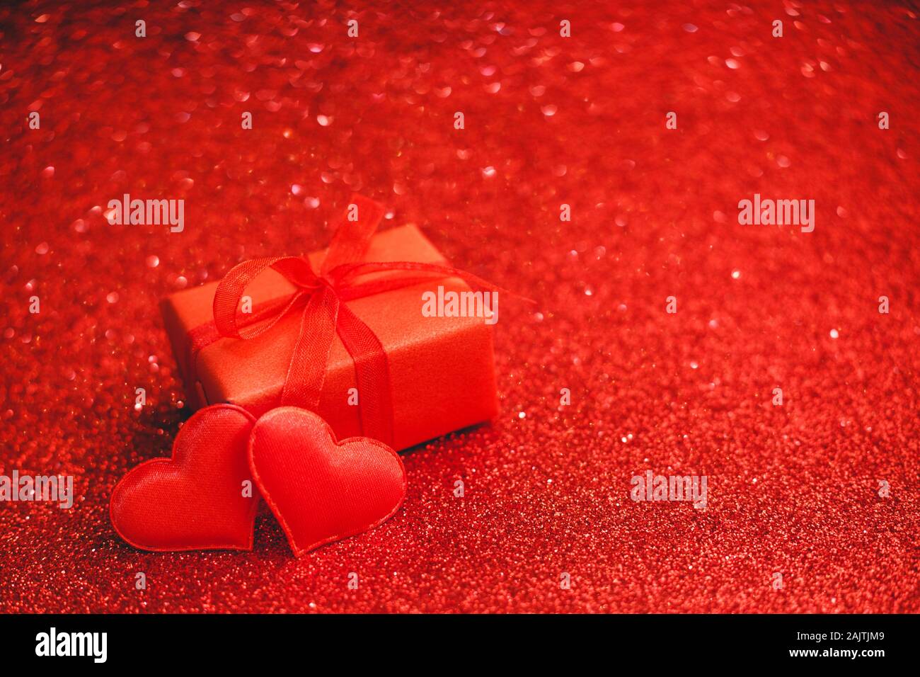 Zwei rote Herzen und roter Geschenkbox auf einem roten Hintergrund der funkelt. Valentines Tag, Liebe, Romantik, Dating, Geschenk, Jahrestag Konzept mit Kopie sp Stockfoto