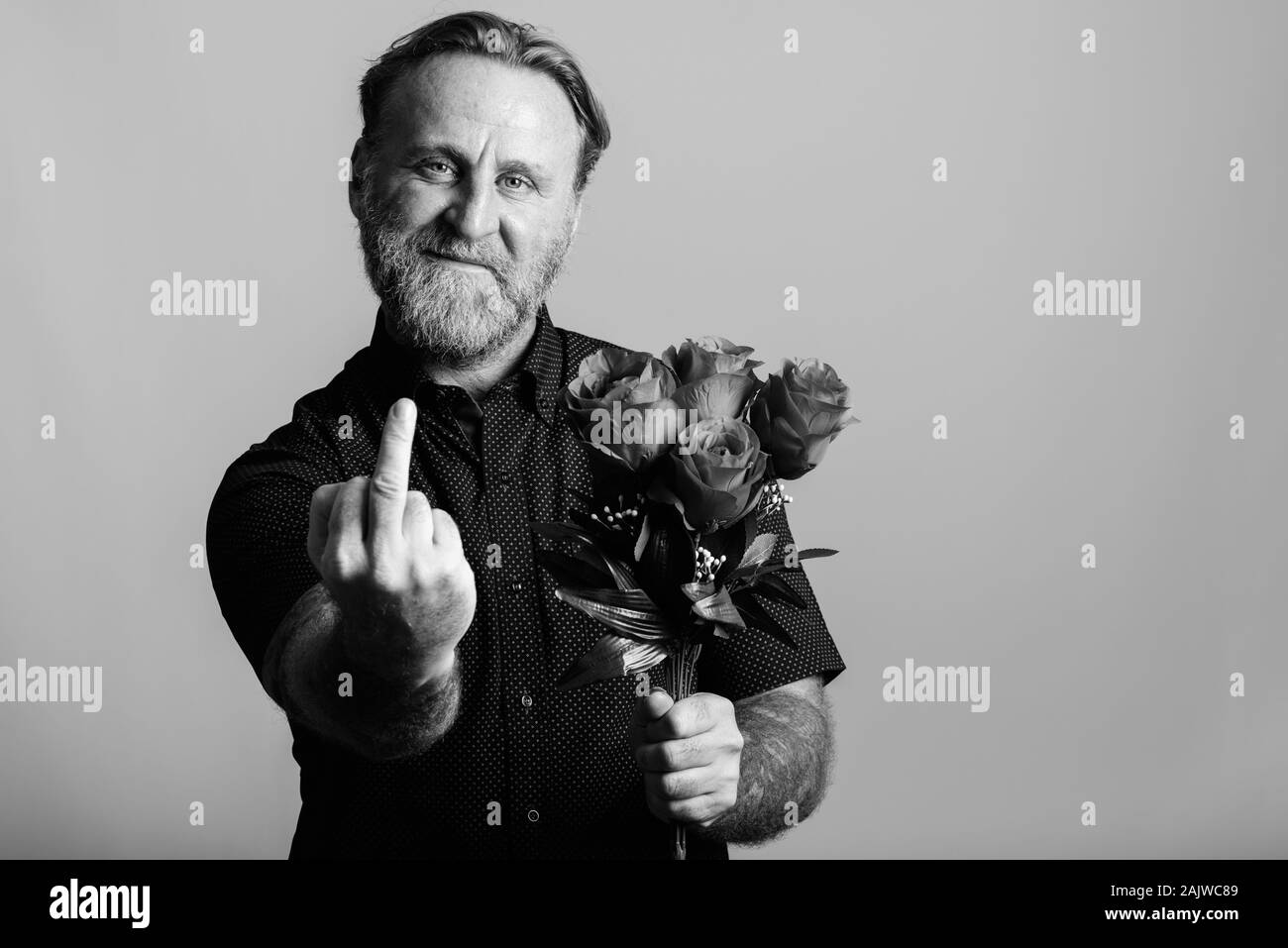 Gerne reife bärtige Mann mit Rosen und zeigt Mittelfinger Stockfoto