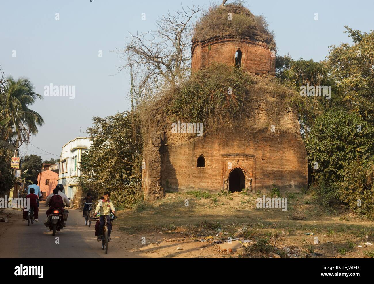 Bishnupur, Westbengalen, Indien - 6. Februar 2018: Eine überwucherte Ruine eines alten Ziegeltempels, der von der Malla-Dynastie erbaut wurde. Kinder fahren auf der Straße, auf der es so ist Stockfoto