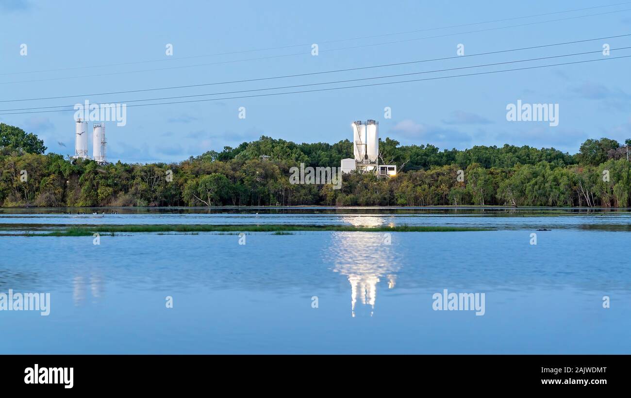 Ein Zementwerk business am Ufer eines Feuchtgebiete Ökosystem bei Sonnenuntergang, mit seinem Spiegelbild im Wasser glänzend Stockfoto