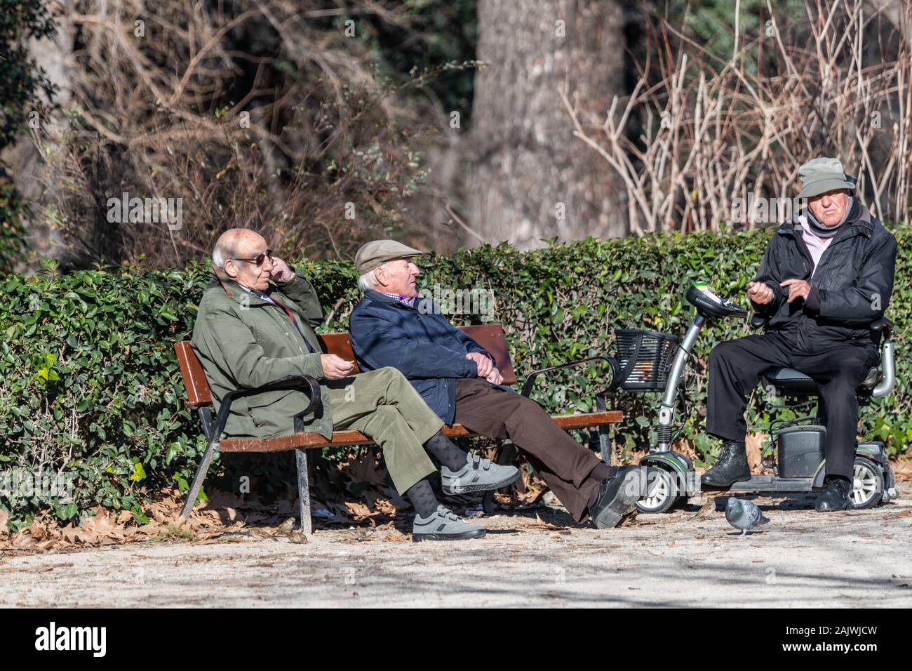 Drei sitzen alte Männer Chat auf eine Bank und eine Invalidität scooter im El Retiro Park, Madrid, Spanien Stockfoto