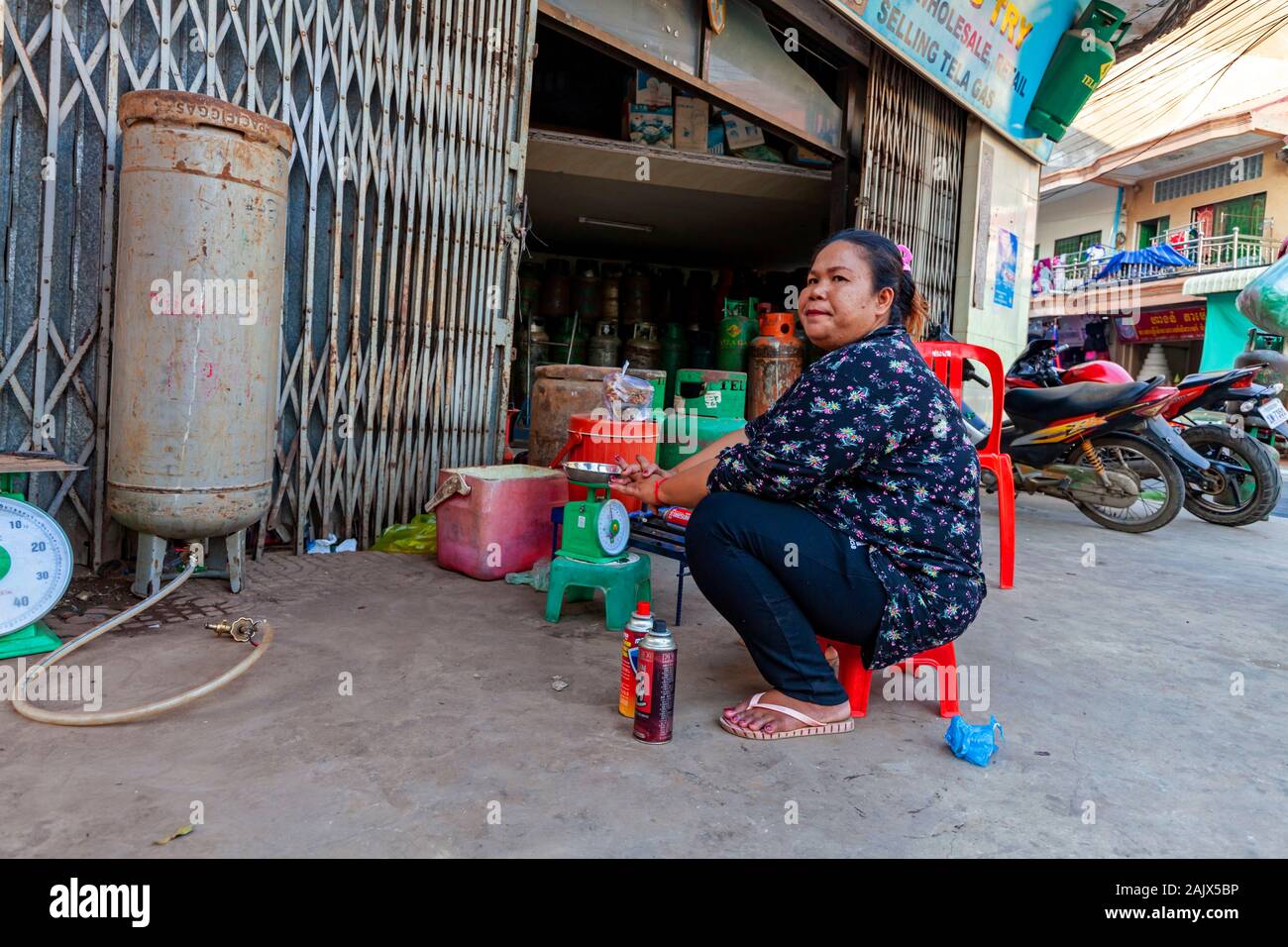 Eine asiatische Frau mittleren Alters arbeitet als Verkäufer im Einzelhandel Propan refill Center auf einem Bürgersteig in einem Geschäft in Kampong Cham, Kambodscha. Stockfoto