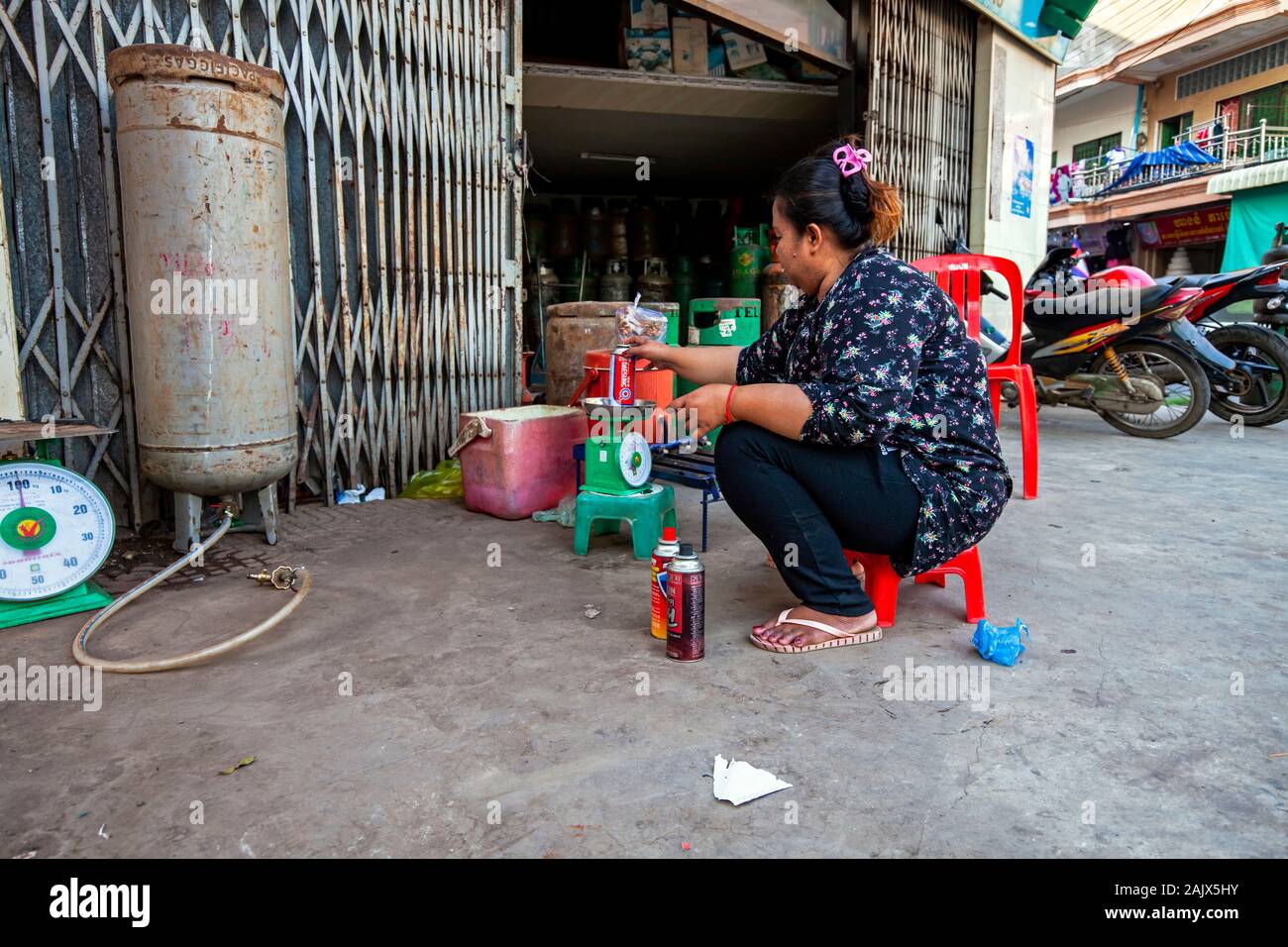 Eine asiatische Frau mittleren Alters wiegt eine gas Kanister im Einzelhandel Propan refill Center auf einem Bürgersteig in einem Geschäft in Kampong Cham, Kambodscha. Stockfoto