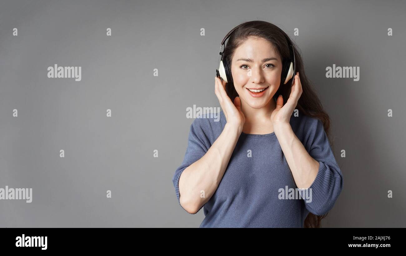 Glücklich lächelnde junge Frau Abspielen von Musik mit drahtlosen Kopfhörern - grauer Hintergrund mit Kopie Raum Stockfoto
