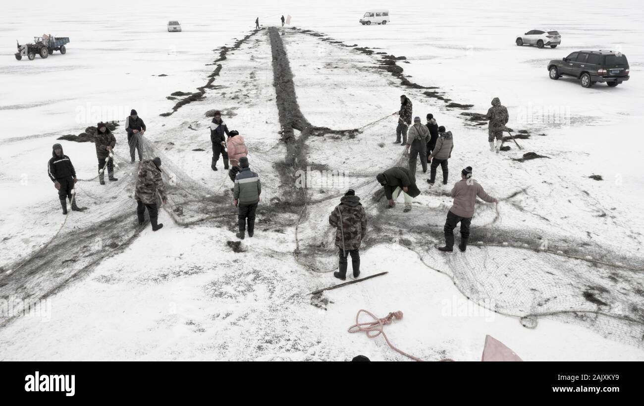 Chinesische Arbeiter ziehen einen riesigen fischernetz Eine gute Ernte auf dem zugefrorenen See in Wolong Kangping County, Shenyang City zu erwarten, im Nordosten Chinas Liaon Stockfoto