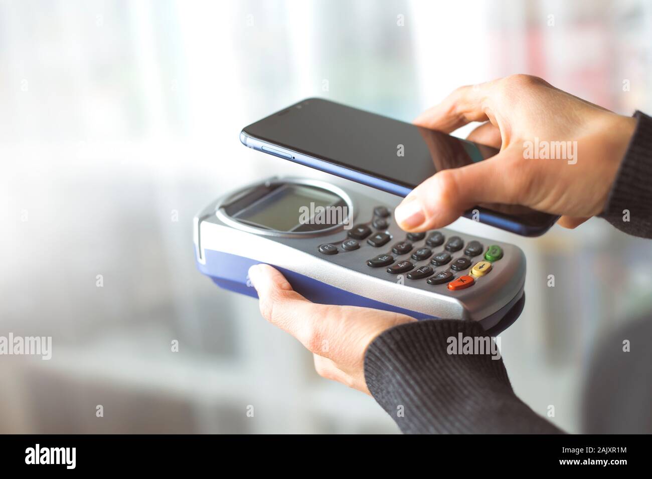 Die Hand des Kunden zahlt sich für das Smartphone im Geschäft mit NFC-Technologie aus. Handy zahlt die Rechnung mit kontaktloser Technologie. Stockfoto