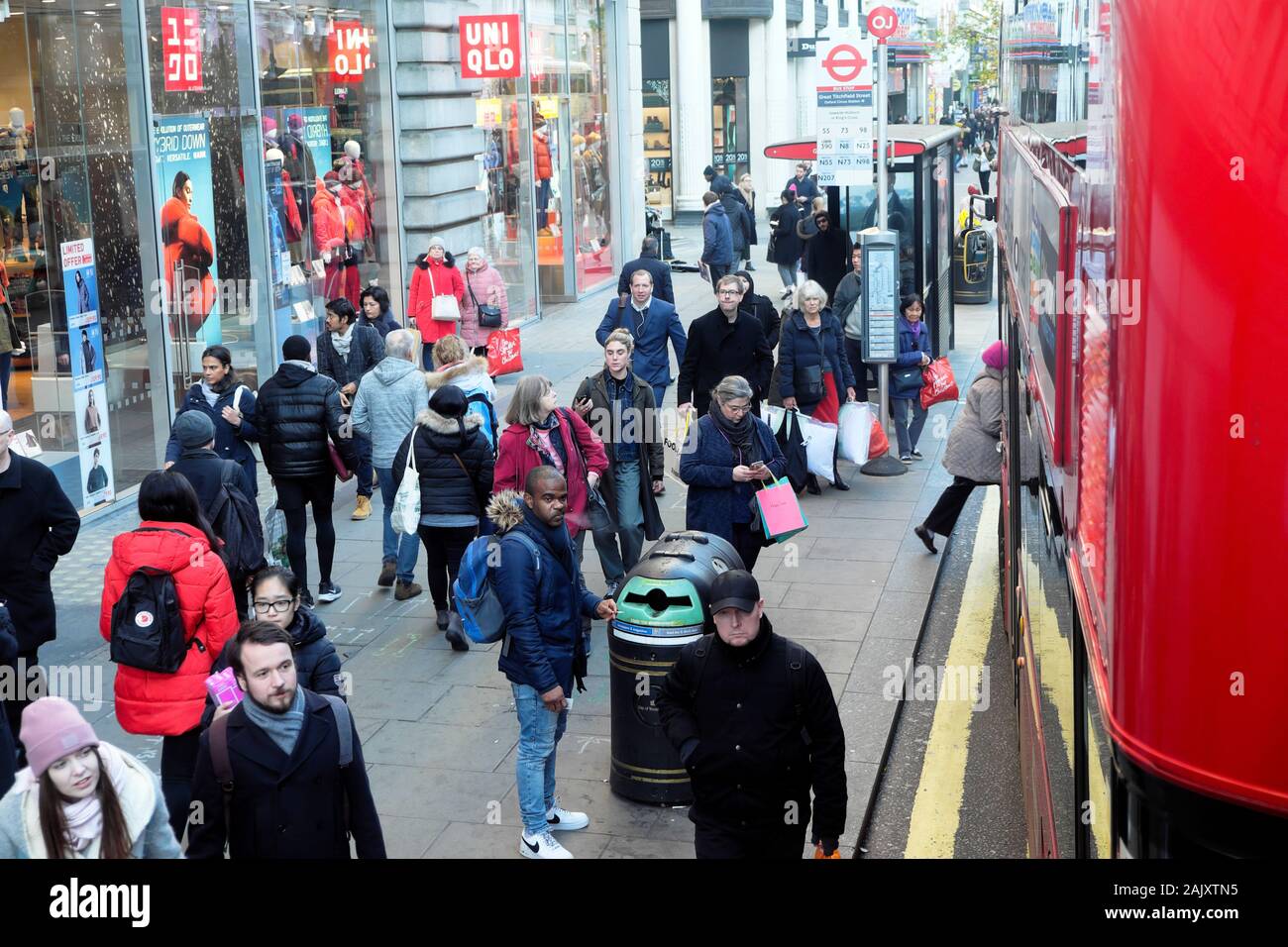 Weihnachtskäufer im Winter Kleidung stehend Warten auf einen Bus an einer Bushaltestelle außerhalb Uniqlo Store in der Oxford Street London England UK KATHY DEWITT Stockfoto