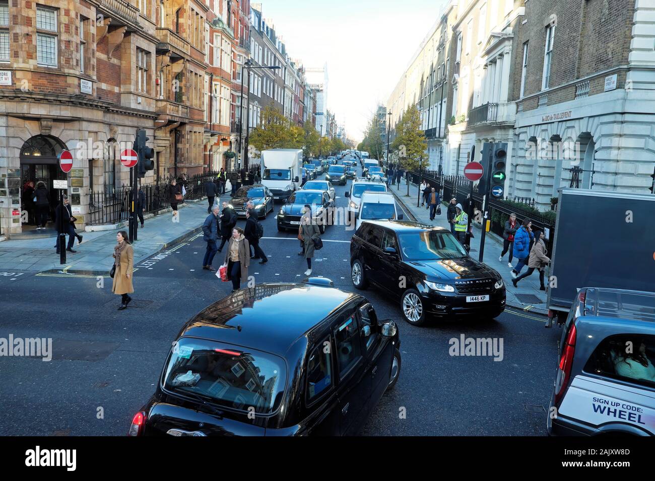 Blick auf der Harley Street Verkehr Taxis, Autos, Fußgänger überqueren von Straßen Einbahnstraßen in Marylebone West London England UK KATHY DEWITT Stockfoto