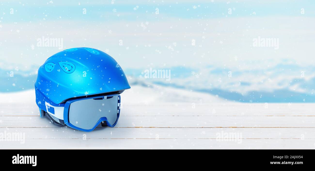 Blue Ski Helm und Brille auf einem weißen Holztisch. Freier Text Platz neben. Schneebedeckten Gipfel der Berge im Hintergrund Stockfoto