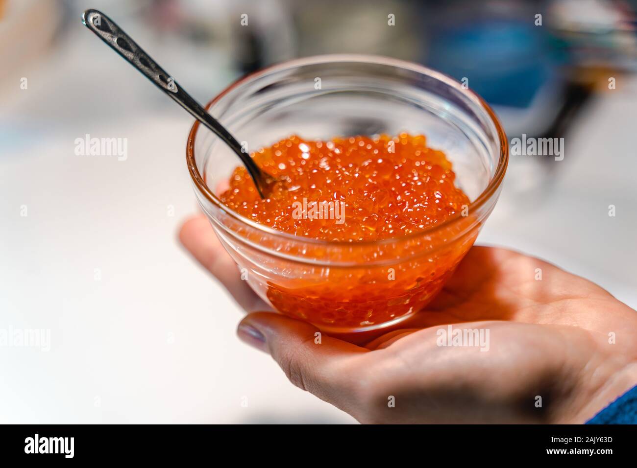 Holding eine Glasschale mit rotem Kaviar. Löffel in der roten Kaviar. Teure Sea Food, Feinkost. Stockfoto