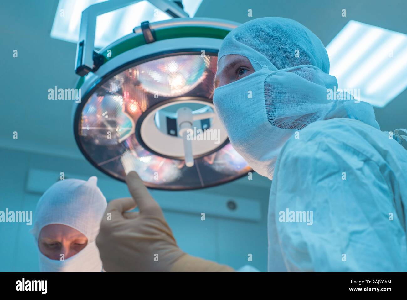 Ansicht von unten der Chirurgen im Operationssaal, in sterilem, Masken, Vorbereitung für chirurgische Interventionen, die Arme angehoben, die in sterilen Handschuhen. Gegen die b Stockfoto