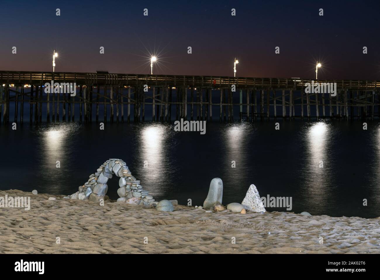 Dawn gestartet über Strand Felsen zart in einen Bogen mit den Lichtern von Ventura Pier leuchtende Lampen gestapelt zu brechen. Stockfoto