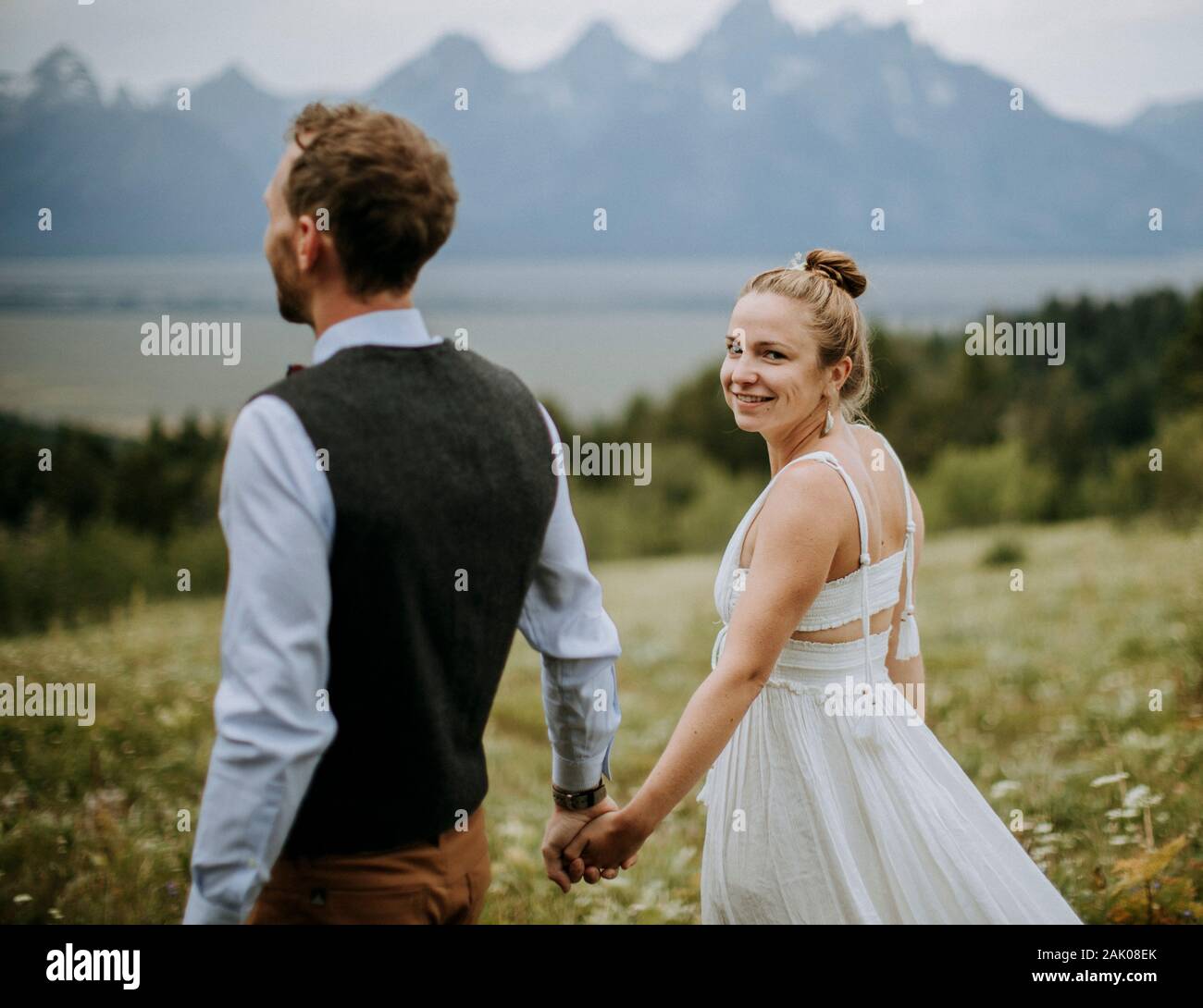 Braut und Bräutigam halten die Hände, während sie durch das Blumenfeld gehen Stockfoto