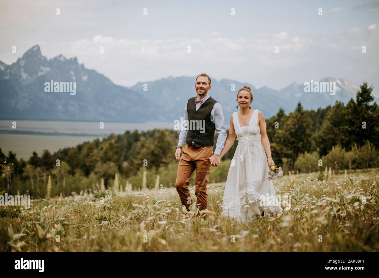 Braut und Bräutigam spazieren durch Wildblumen vor den Teton Bergen Stockfoto