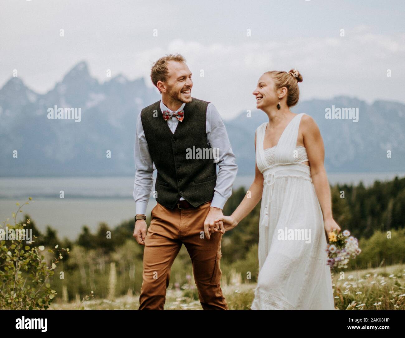 Lachende Jungvermählte halten die Hände, die in den felsigen Bergen Wyoming spazieren Stockfoto