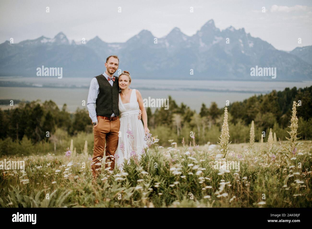 Brautpaar und Brautpaar Brautpaar lächeln und umarmen sich im Feld der Wildblumen Stockfoto