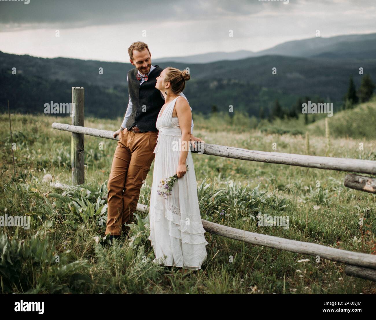 Frisch vermählte sehen sich an und lächeln, während sie sich auf einen Zaun lehnen, Wyoming Stockfoto