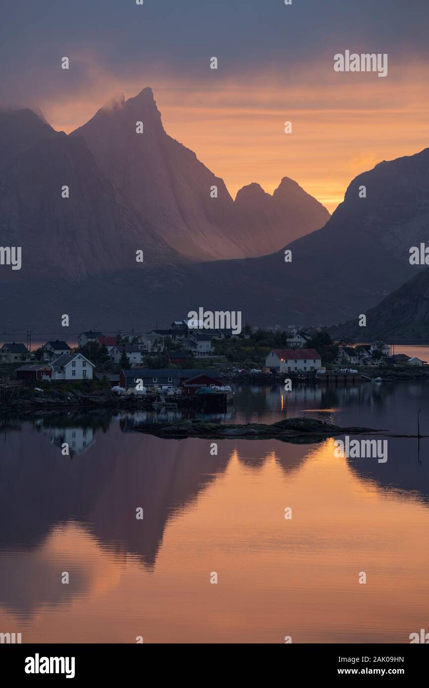 Juni buntes Licht der Mitternachtssonne scheint durch Mountain Pass hinter fjordside Dorf, Reine, Moskenesøy, Lofoten, Norwegen Stockfoto