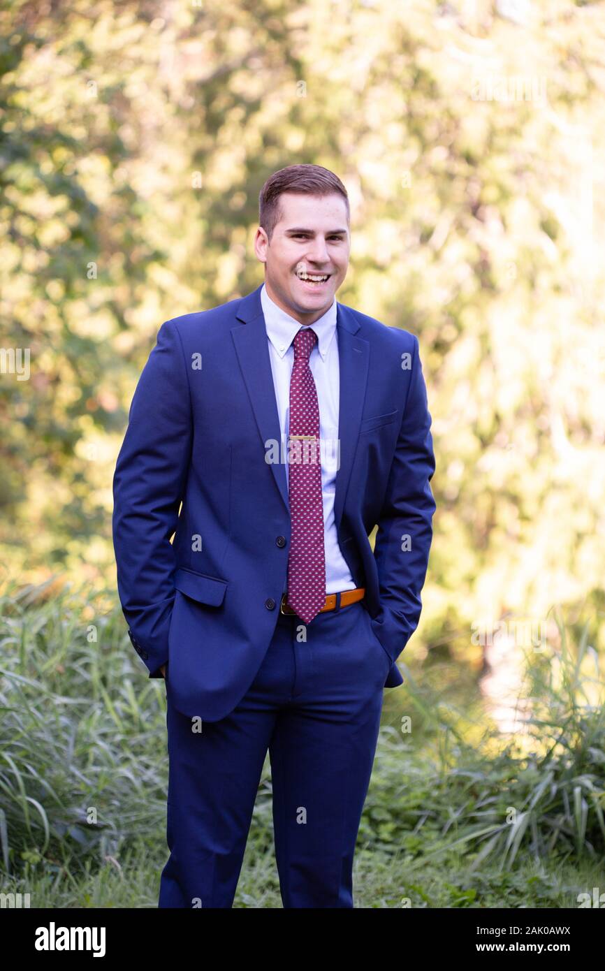 Junger Mann im Business-Anzug steht draußen und lacht selbstbewusst. Stockfoto