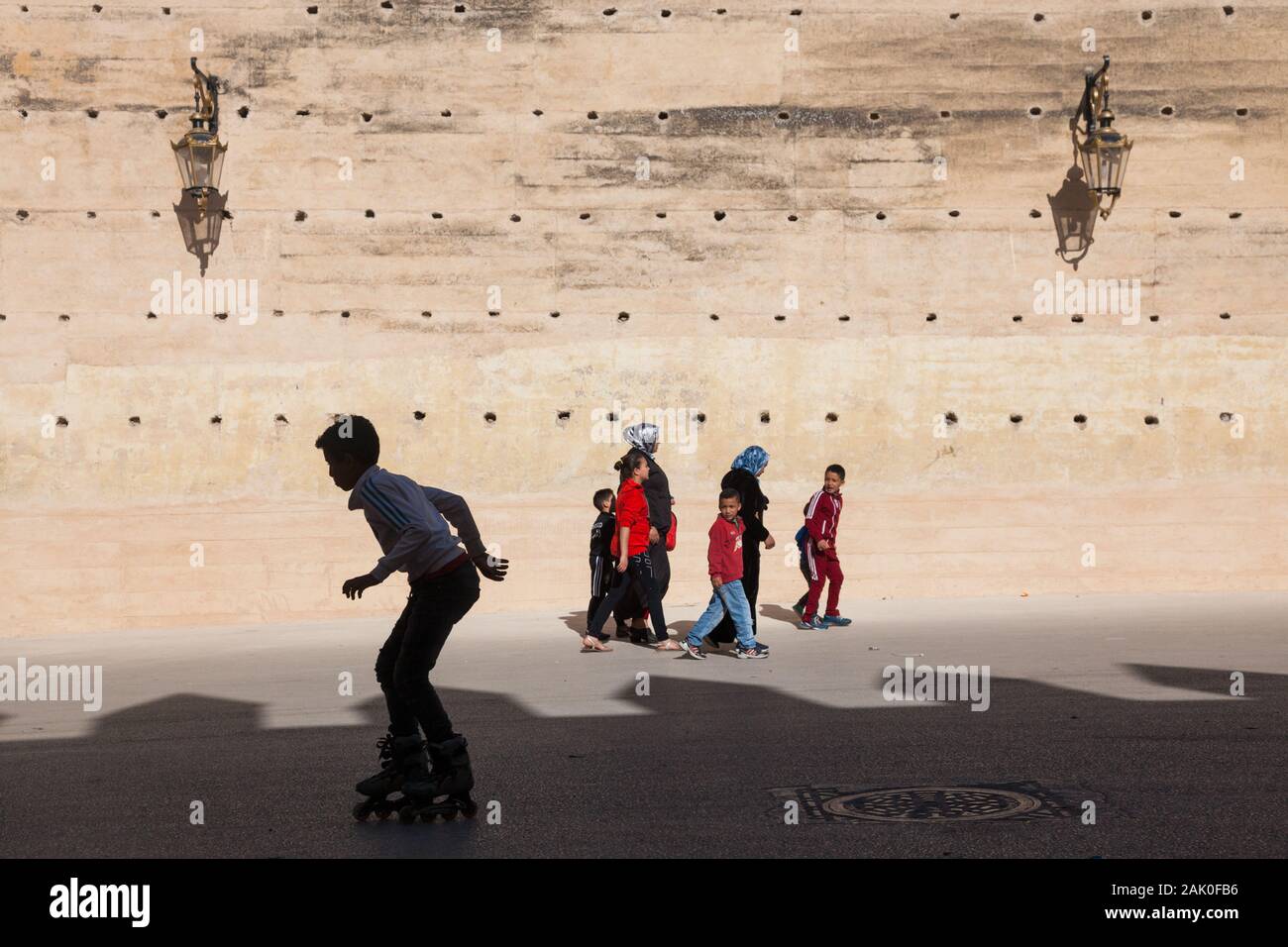 Tradition und Moderne - Junge auf Inline-skates und Fußgänger (Frauen und Kinder) am Nachmittag Landschaft der Stadtmauer in Fes (fès), Marokko Stockfoto